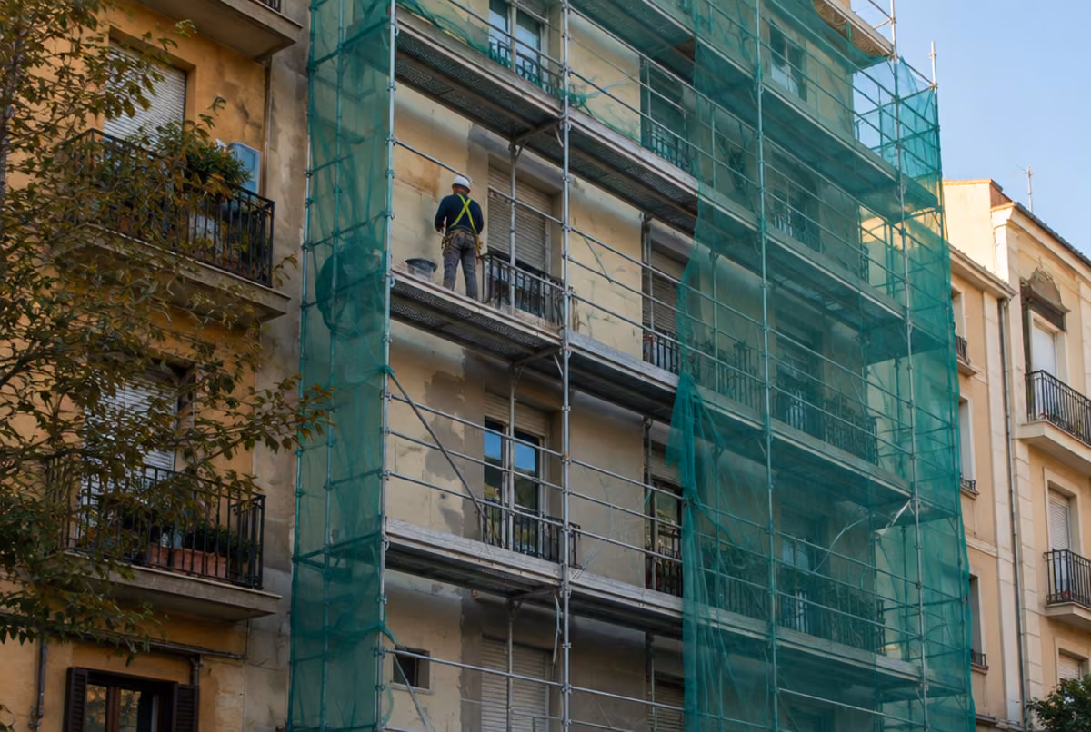 Edificio de viviendas con andamio y red de seguridad durante la rehabilitación de la fachada